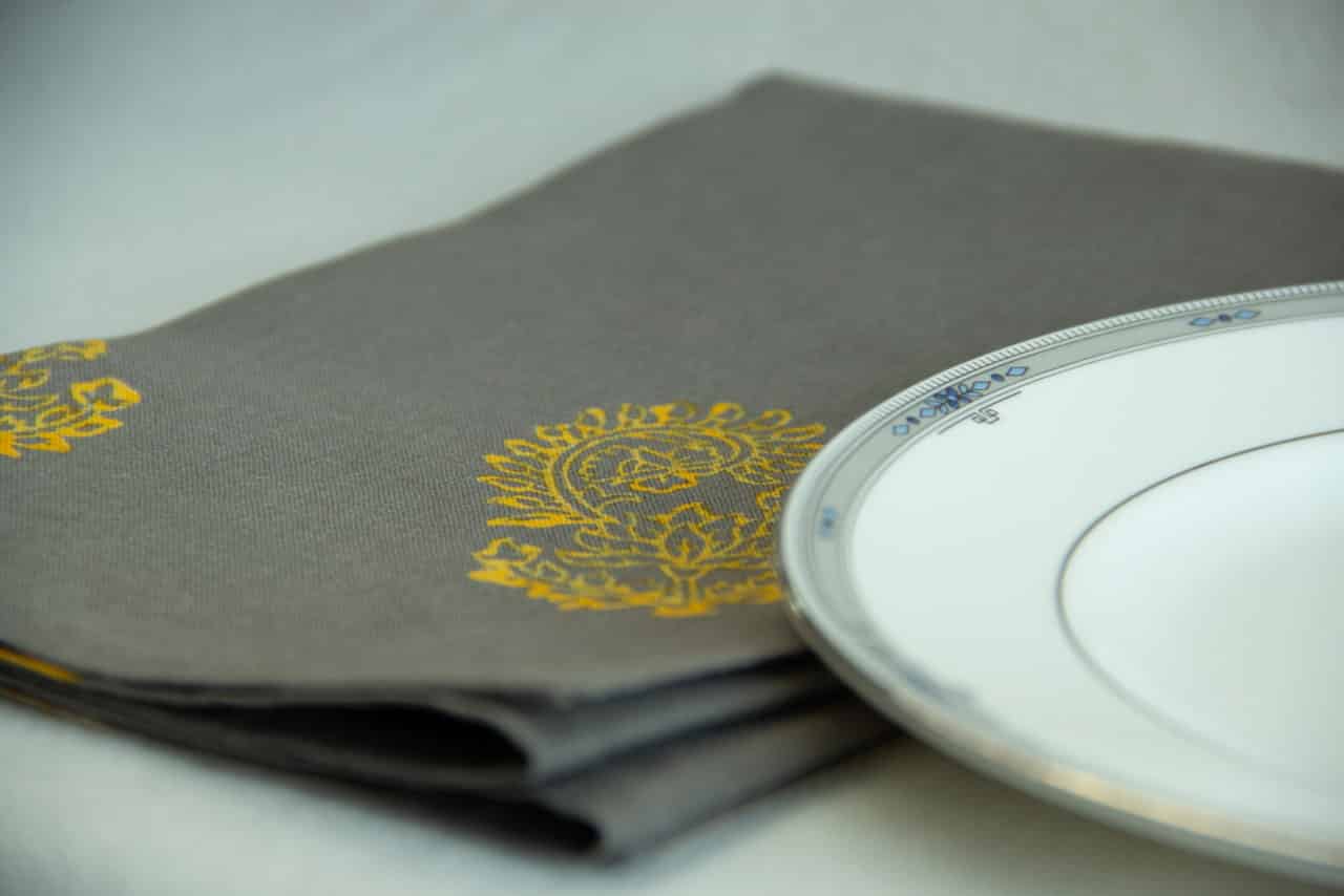 Grey table napkin with yellow floral print, placed next to a white plate