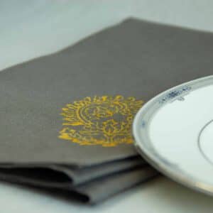 Grey table napkin with yellow floral print, placed next to a white plate