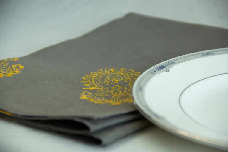 Grey table napkin with yellow floral print, placed next to a white plate