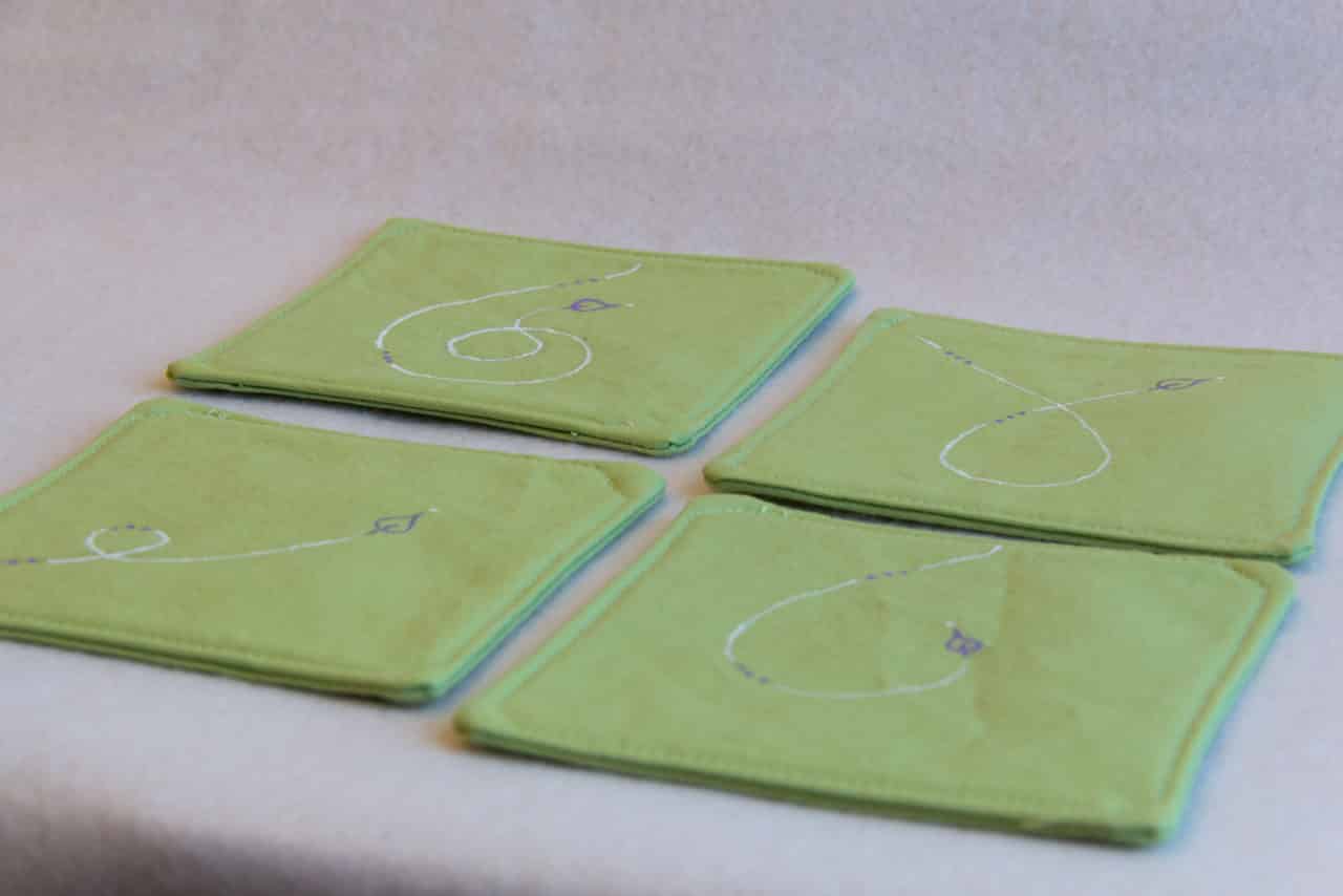 Four coasters with white and purple designs on a green background