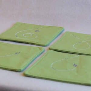 Four coasters with white and purple designs on a green background