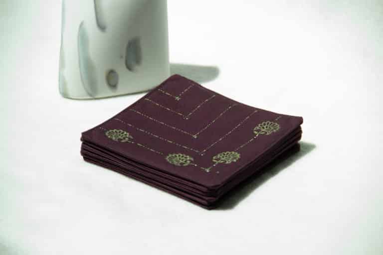 Stack of eggplant colored coasters next to a decorative stone.