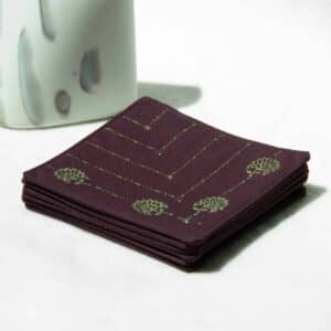Stack of eggplant colored coasters next to a decorative stone.