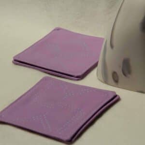 Four lavender colored coasters with fluorescent blue dots next to a decorative stone