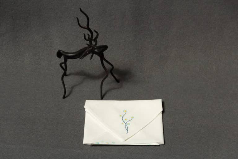 A folded handkerchief with a hand-painted floral design next to a small statue of a horse