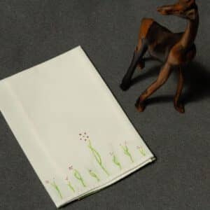 A folded handkerchief painted with small plants with plum colored flowers, next to a small wooden giraffe