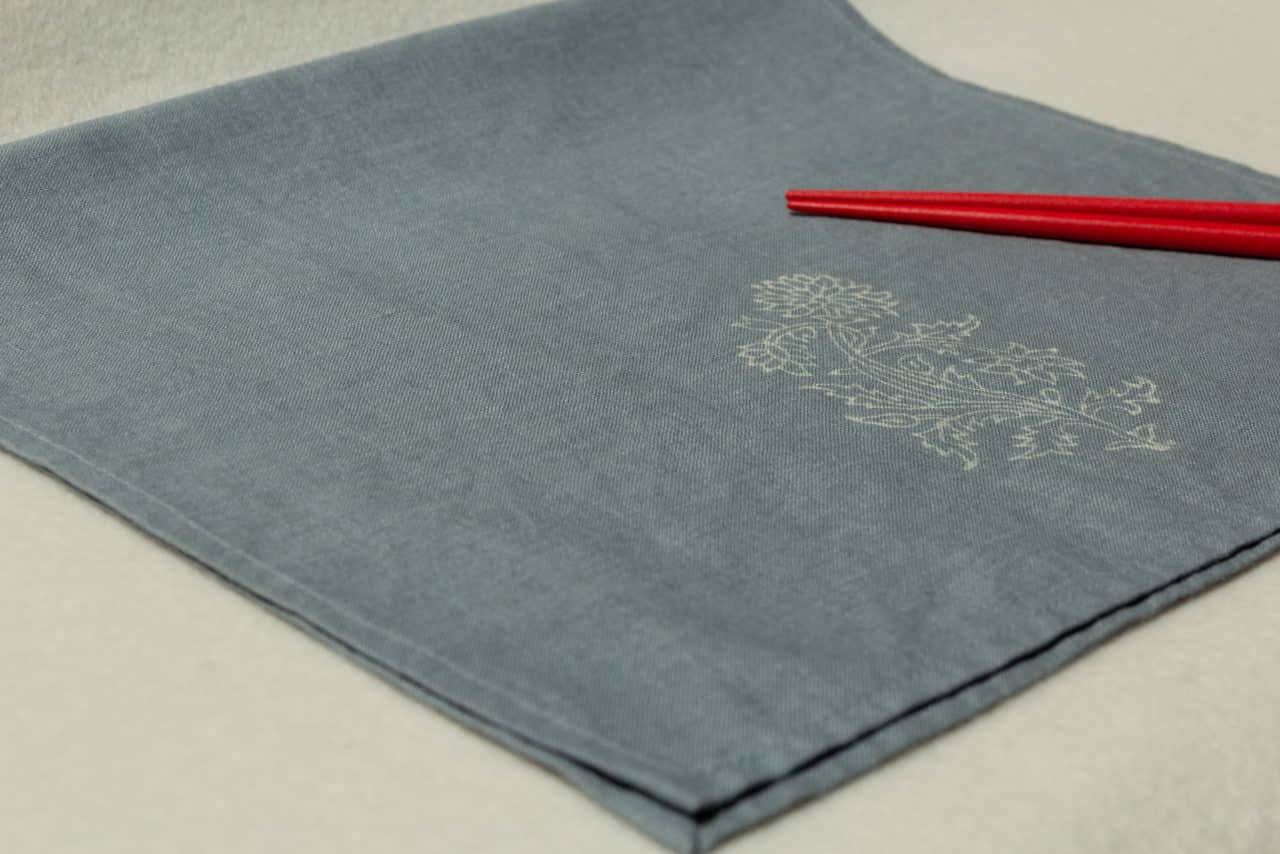 Blue-gray linen hand towel with floral print, and two red chopsticks