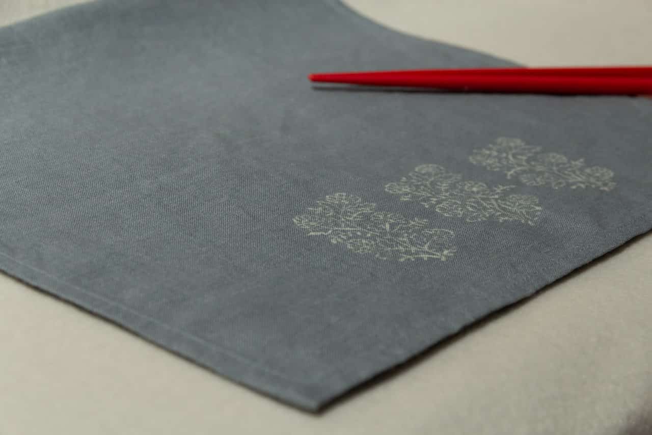 A blue-gray linen napkin with vintage block prints, and two chopstick.
