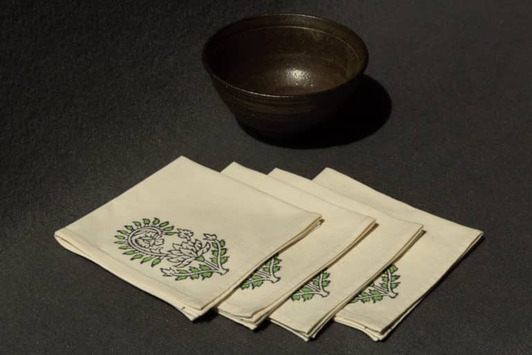 Four napkins with a woodblock print next to a ceramic bowl