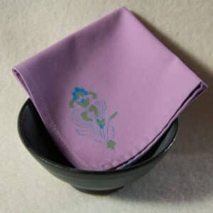 A lilac colored cocktail napkin with a blue and green floral print folded inside a bowl.