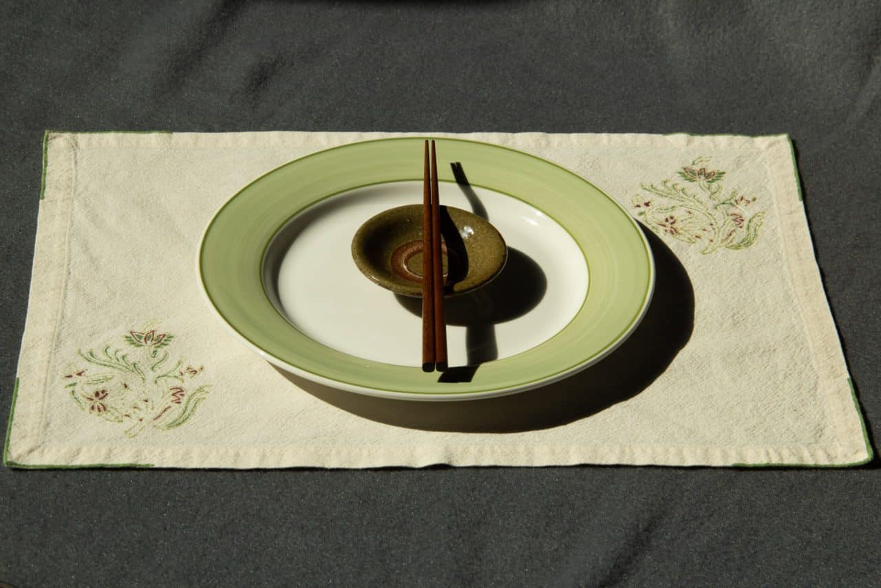 A plate, dipping bowl and chopsticks kept on top of a placemat.