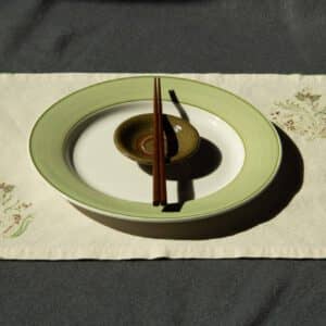 A plate, dipping bowl and chopsticks kept on top of a placemat.
