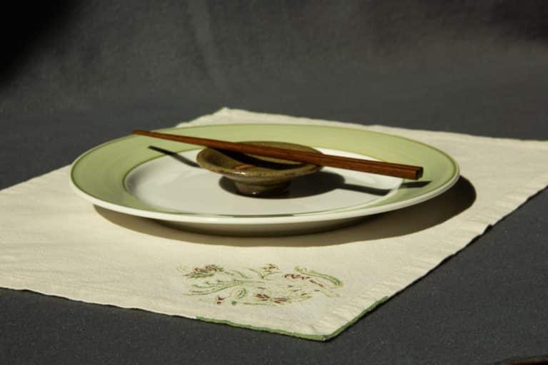 Off-white placemat with woodblock printed pattern, shown with a plate, sauce cup and chopsticks on top.