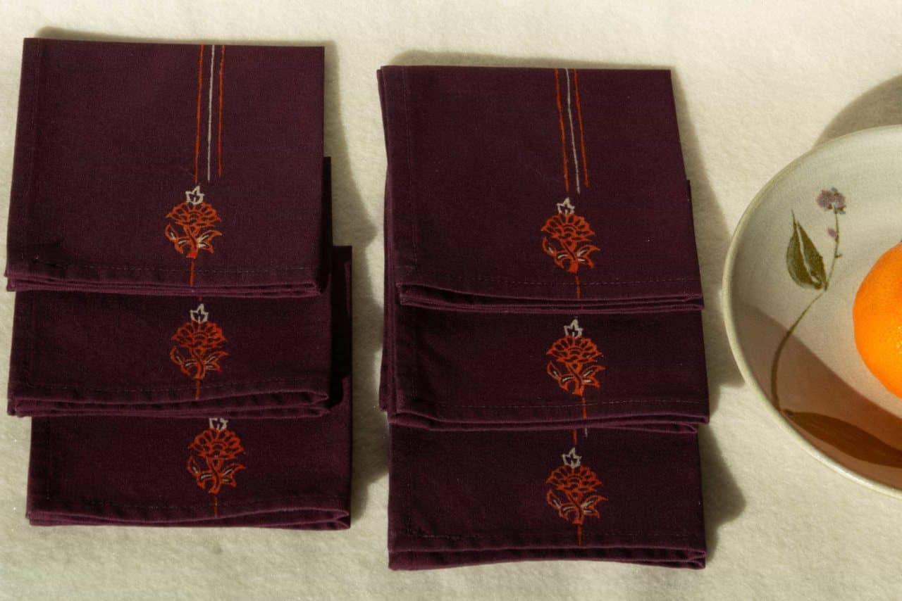 Six folded cocktail napkins next to a small plate with an orange