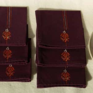 Six folded cocktail napkins next to a small plate with an orange
