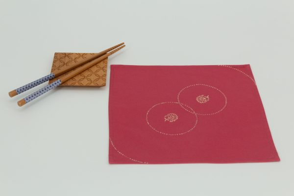 A single napkin next to a wooden coaster and two wooden chopsticks arranged on the coaster