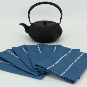 Six folded napkins arranged in a fan shape next to a cast iron kettle