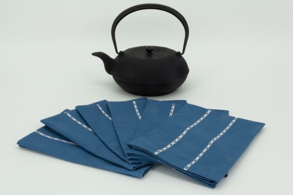 Six folded napkins arranged in a fan shape next to a cast iron kettle