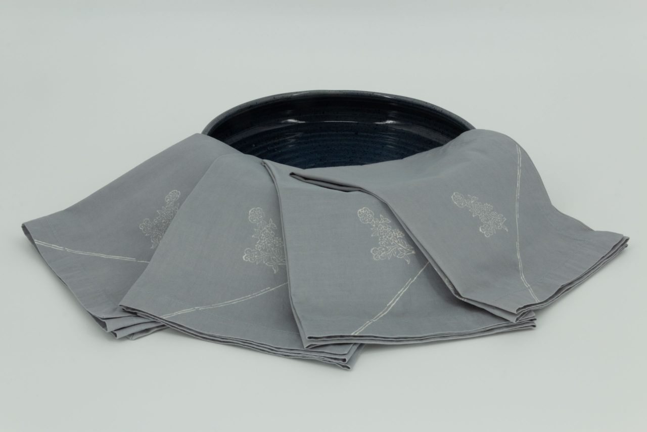 Four folded napkins draped over a wide ceramic dish