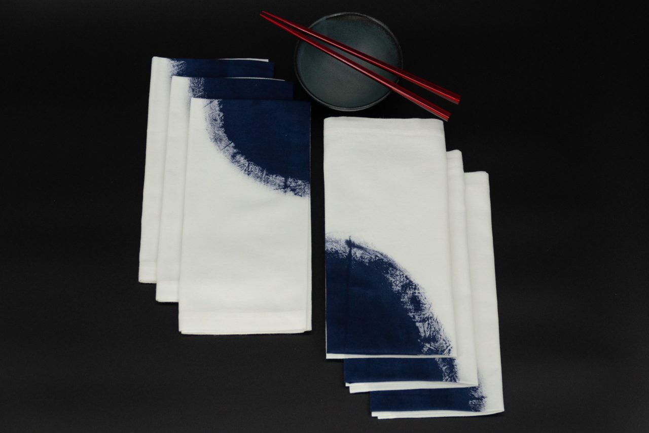 Six folded napkins next to a ceramic bowl and two chopsticks
