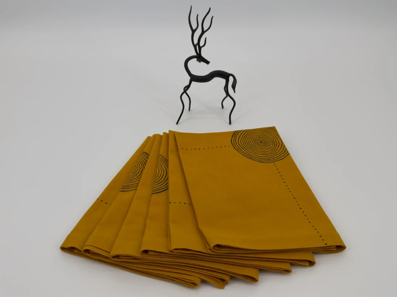 Six napkins folded and placed next to a small metal image of a deer