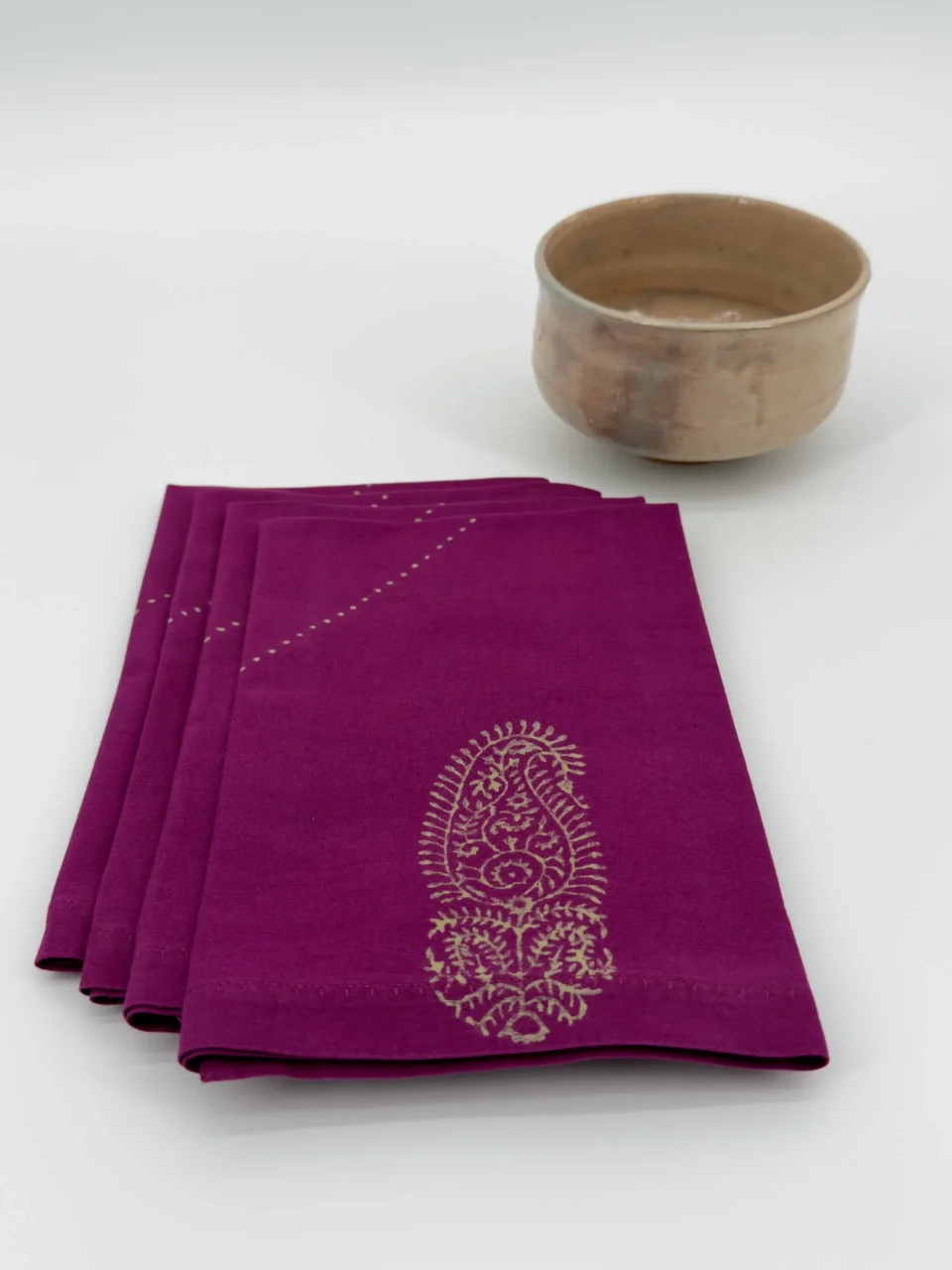 A set of four folded napkins next to a ceramic bowl