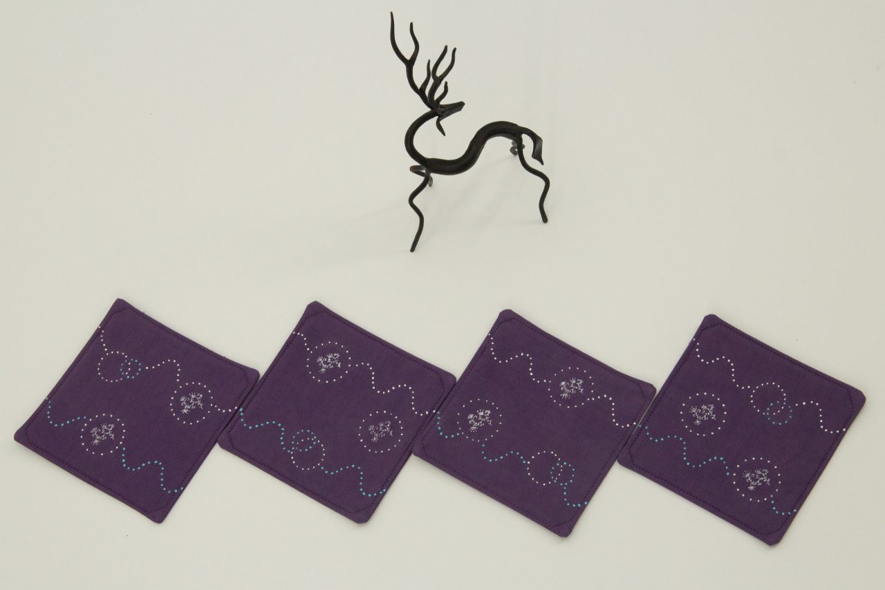 Four coasters next to a small metal sculpture of a deer