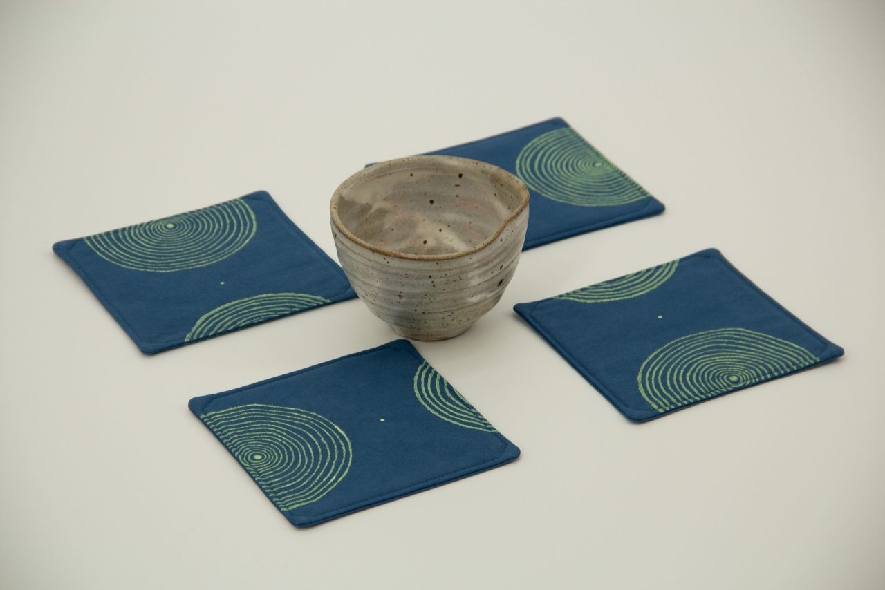 A set of four coasters with a ceramic cup in the middle